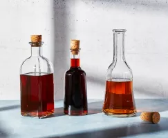Three glass bottles of brown sugar simple syrup on a counter, two corked and one uncorked