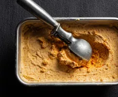 Carrot ice cream in a metal tin with an ice cream scoop