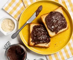 Cocoa tahini spread on two slices of toast, on a yellow plate with a knife