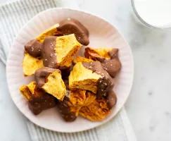 A bowl of chocolate coated sponge toffee on a bowl with a glass of milk