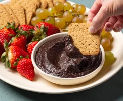 Bowl of chocolate hummus on a platter with graham crackers, figs, strawberries, and grapes