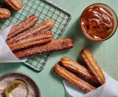   Churros with cinnamon sugar on a wire cooling rack with a bowl of dulce de leche dip