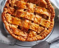 Lattice-topped apple pie on a cooling rack with a pie server