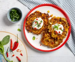 Sweet Chili Corn Fritters on a red and white plate with sour cream and herbs