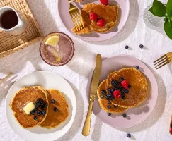 Three plates of easy fluffy pancakes in a picnic setting, with fresh berries, butter and maple syrup