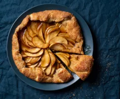 Baked apple galette with one slice cut on a blue plate on a tablecloth