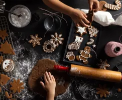 An assortment of gingerbread cut-out cookies on a cooling rack, counter, and pan with icing and decorating equipment