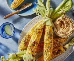  Grilled corn on the cob on a platter with a bowl of chipotle-lime butter, shown with a glass of ice water with a slice of lime
