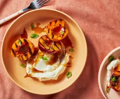 Two bowls of grilled peach halves with mascarpone and basil garnish and brown sugar glaze