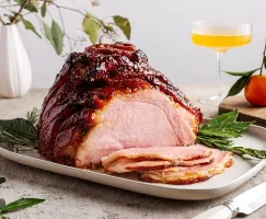 Roasted glazed ham on a platter and garnished with herbs with several slices cut