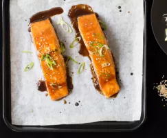 Two pieces of Lacquered Salmon with Crispy Skin on baking sheet with parchment paper