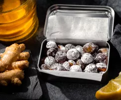 Homemade cough drops in a tin beside lemon slices, ginger root, and honey