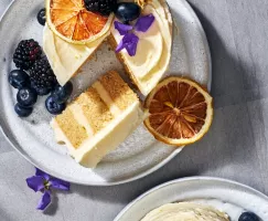 A miniature lemon chamomile cake on a plate with a slice cut, served with berries and topped with berries, edible flower petals,