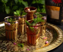 Five colourful glasses of Moroccan mint tea garnished with mint leaves on a gold platter