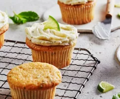 Mojito cupcakes on a wire cooling rack, some topped with ermine frosting and garnished with lime.