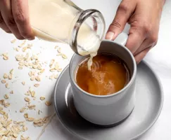 Pouring vanilla oat beverage into a mug of coffee from a glass bottle