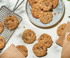 Soft oatmeal raisin cookies on a plate, a cooling rack, a table, and in paper sleeves