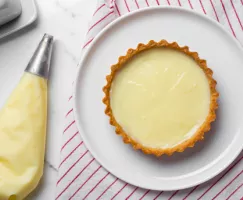 A piping bag beside a tart filled with cream