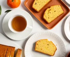Slices of orange pound cake on plates with a cup of tea and an orange