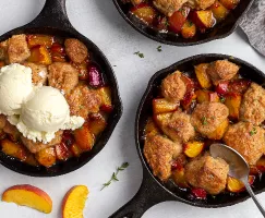 Three peach cobblers served in cast iron frying pans, one with vanilla ice cream