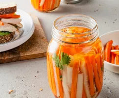 A jar of pickled carrots and daikon radishes with a sandwich in the background