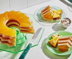 Piña Colada Layered Gelatin Dessert on a green glass stand, with two slices cut and served on mismatched green plates.