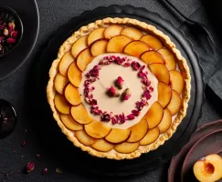 Plum custard tart decorated with sliced plums and dried rose petals on a black platter on a black table