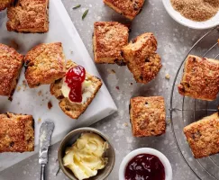 Vanilla rosemary date scones on a platter and a cooling rack shown with dishes of butter and jelly and a bowl of turbinado sugar