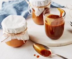Three glass jars of salted butterscotch sauce, one open and two covered with cloth and tied off with twine.