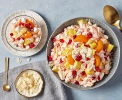 A large bowl of Ambrosia salad shown with a single serving in a glass bowl and a plate of shaved coconut