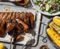 A platter of ribs with mustard barbecue sauce with salad and barbecued corn on the cob