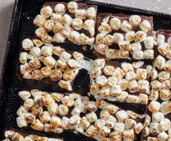 S’mores bars in a black and gold serving tray, with toasted marshmallows partially melted and stretched.