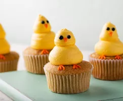 Cupcakes decorated with yellow chicks made of piped icing, on a green wood board
