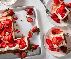 A strawberry-yuzu sheet cake on a white tray served with strawberries, shown with two slices on plates.