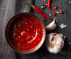 Metal bowl of sweet chili sauce with whole and cut chilis and a clove of garlic