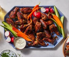 A platter of sweet and spicy grilled chicken wings served with raw vegetables, dip, and sparkling beverages