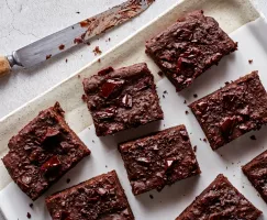 Vegan brownies topped with dark chocolate chunks on a platter with a knife.