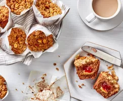 Vegan Peanut Butter and Jam muffins on a breakfast table, some wrapped in paper in a basket and one cut open on a plate and serv