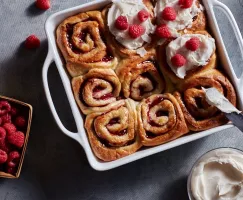 Fresh vegan raspberry cinnamon rolls in a baking dish, some bare, some with coconut glaze and raspberries