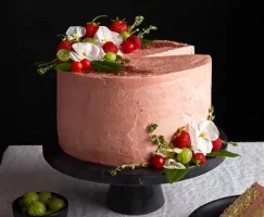White Wine Celebration Cake on a cake platter with strawberries, flowers and a slice missing
