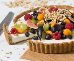 Yogurt Fruit Tart with Granola Crust topped with various fruit and granola sitting on a piece of parchment paper