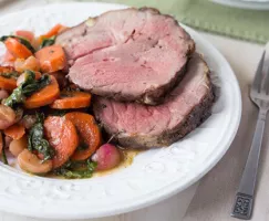 White plate with two slices of mint glazed lamb and candied vegetables