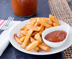 Table setting with plate, napkin and fork. French fries on the plate with ramekin of ketchup. 