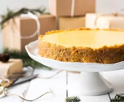 Cheesecake on a cake platter surrounded by presents wrapped in brown paper