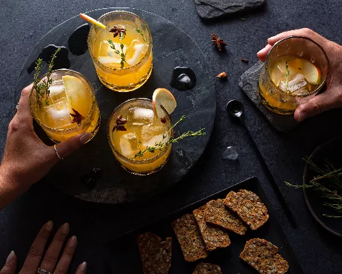 Hands reaching for glasses of Pumpkin Spice rum cocktail, served with crackers