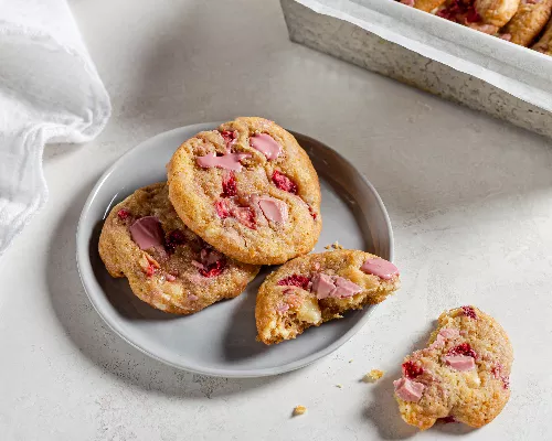 Three strawberry and ruby chocolate chunk cookies on a plate, one broken in half