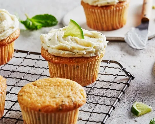 Mojito cupcakes on a wire cooling rack, some topped with ermine frosting and garnished with lime.