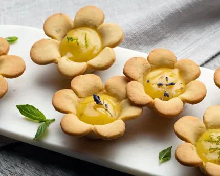 Flower-shaped tart with a lime-lavender curd in the middle decorated with lavender and mint leaves
