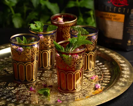 Five colourful glasses of Moroccan mint tea garnished with mint leaves on a gold platter